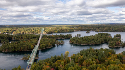 Fototapeta premium Aerial view of the Thousand Islands Bridge spanning over lush green islands and blue waters in the Thousand Islands region. This iconic bridge connects islands in Canada and the United States, showcas