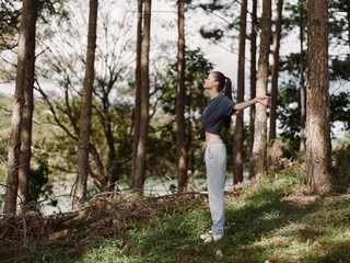 Relaxed young woman enjoying nature in forest, practicing yoga with arms outstretched, surrounded by trees and greenery Mindfulness and wellness concept
