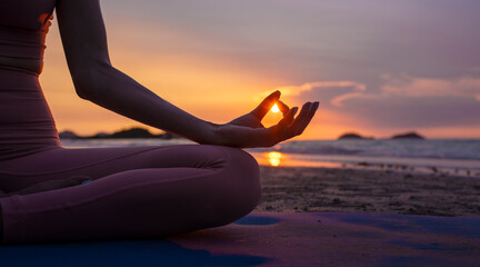 Silhouette of sport woman performing a yoga pose on the beach at sunset, with the sun setting behind the horizon and the calm sea .Yoga is meditation and healthy sport relaxing on summer holiday