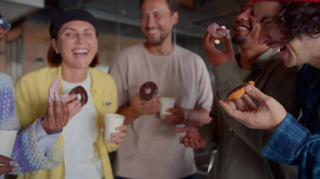 Happy colleagues enjoy break eating chocolate donuts in office