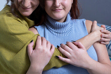 Two women embracing affectionately while wearing cozy sweaters in a modern indoor setting. Female connection concept. Close up. Unrecognizable faces.