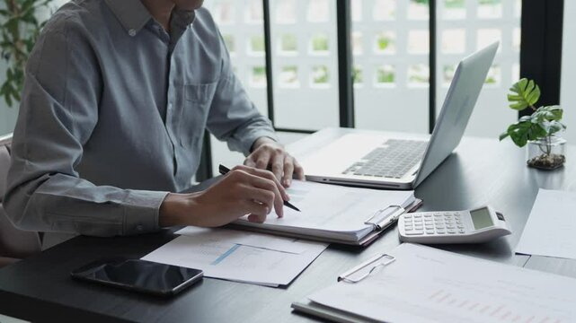 Businessman sits on chair holding pen and checking documents