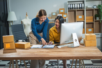Two Asian business woman work at desk, selling fashion clothes online. They are packing checking...