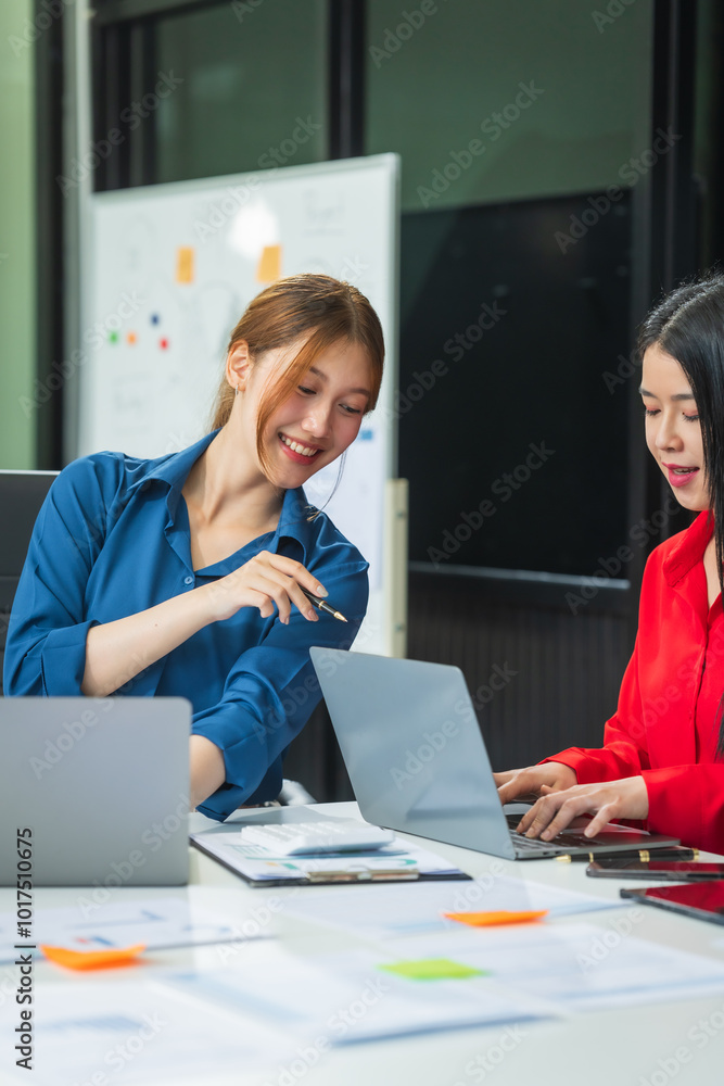 Wall mural two asian business woman work at a desk, discussing business strategies, marketing, plans.they analy