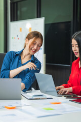 Two Asian business woman work at a desk, discussing business strategies, marketing, plans.They...
