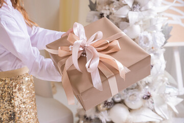 Hands with wrapped christmas gift with white bow on background of christmas tree lights. Stylish...