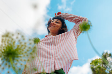 girl in a pink shirt moves in the blue sky. Portrait of a young girl enjoying nature outdoors in a field with flowers.