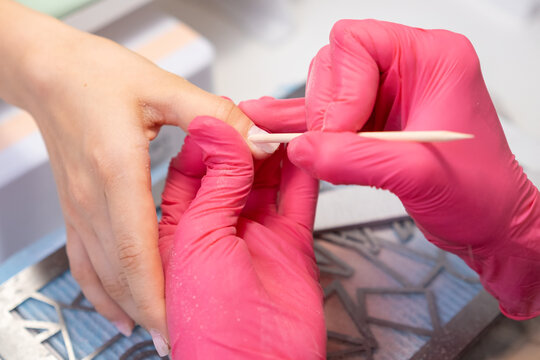 Close up manicure master uses an orange stick to remove cuticula pro clients fingers. 