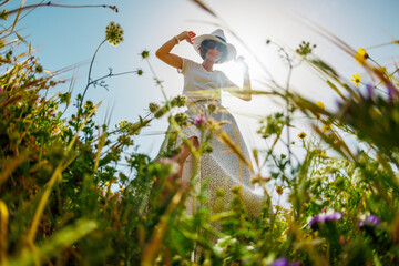 Summer mood. a young and cheerful girl posing against a background of blue sky and flowers. A...