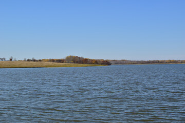View of the lake. In the distance are meadows with forest.