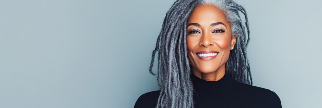 A mature woman with gray dreadlocks smiles brightly at the camera in a portrait.