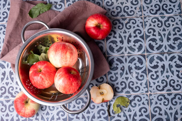 Ripe red apples lie in a metal colander on a table .