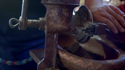 A hand performs the traditional process of grinding coffee beans in an artisanal way. The image captures the connection between manual work and the quality of the coffee, highlighting the dedication