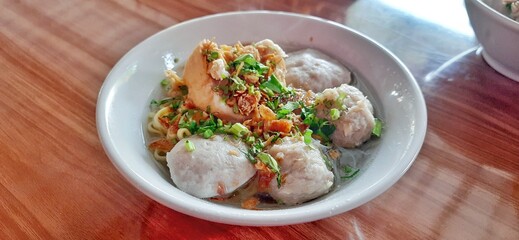Bakso Sapi Gepeng. Popular street food dish of flat meatball soup served with noodles, lime, sauce, vegetables. Indonesian cuisine background