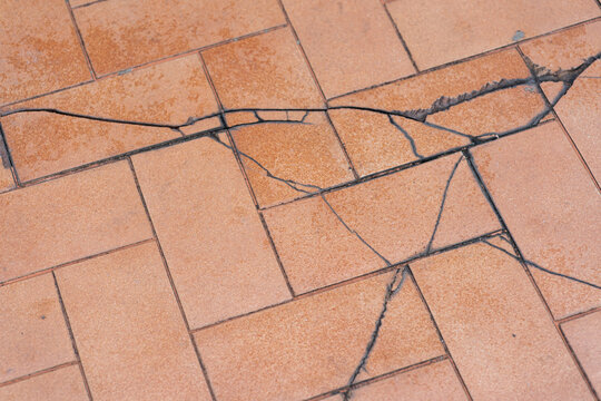 Broken floor. Tile with large diagonal cracks and chips. Problems of the construction of houses, collapse houses, soil collapsed, tiles broken damaged, floor split. cracked floor tiles, house damaged.