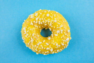 Yellow donut with icing on blue background, close-up, top view.