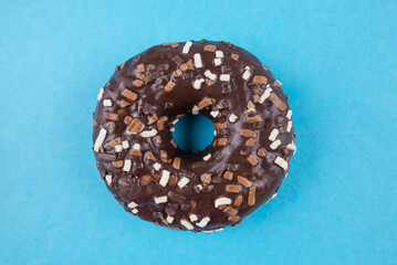 Chocolate donut with glaze on blue background, close-up, top view.