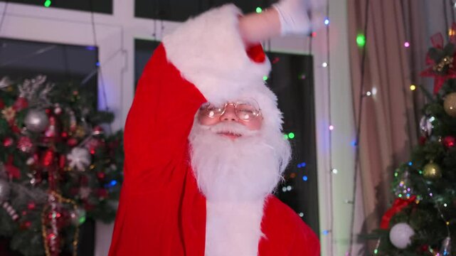 Bearded Santa Claus waves hand with Italian flag at Xmas party against background of festive decorations of Christmas tree and twinkling garlands. 