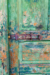 Detail of a wooden door with a rusty bolt. Green peeling paint. The wood grain is visible.