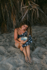 Woman holding large abalone shell on beach under palm trees