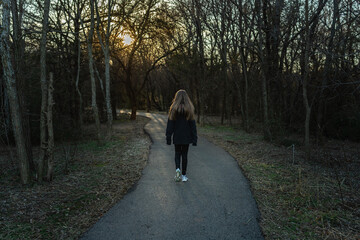 A girl walking paved path at sunset, surrounded by bare trees