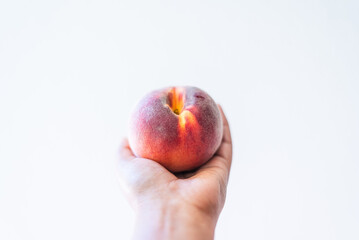 A hand holding a ripe peach against a clean, white background.