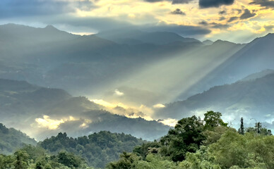 The sunlight penetrates the clouds, shining down on the mountain peaks, creating shimmering,...