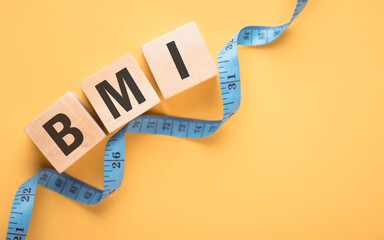 Wooden block displaying 'BMI' next to a measuring tape on yellow background. The concept of Body...
