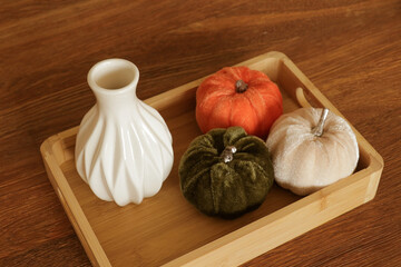 Wooden box with pumpkins, light beige plaid, orange velvet pillow and boho pillow with fringe lying on bed with white linen. Home decor. Cozy fall bedroom. Autumn decoration.