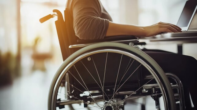 Close-up of a woman's hand using a laptop while sitting in a wheelchair.