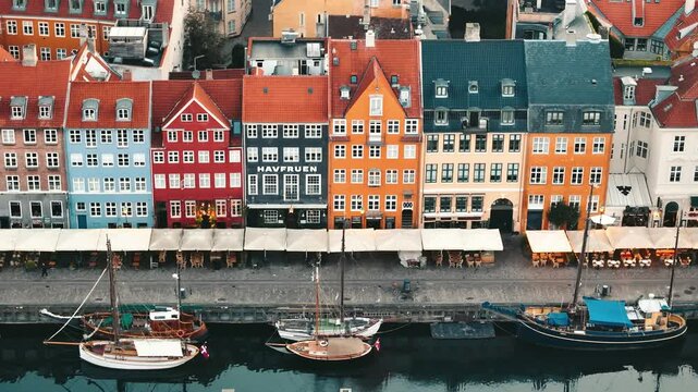 Tracking aerial view of Nyhavn canal at sunrise with boats and glowing buildings in Copenhagen