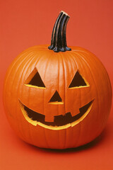 A pumpkin with a smiley face carved into it. The pumpkin is orange and has a black stem