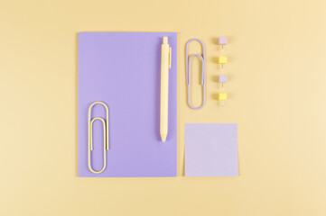 Top view of purple notebook on yellow background. Sticky note, paperclips, pen and pins. School, office wallpaper. Flat lay, copy space.