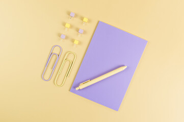 Top view of purple notebook on yellow background. Paperclips, pen and pins. School, office wallpaper. Flat lay, copy space.