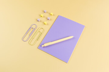 Top view of purple notebook on yellow background. Paperclips, pen and pins. School, office wallpaper. Flat lay, copy space.