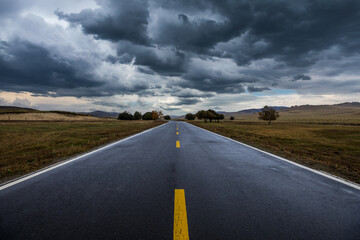 Naklejka premium Asphalt highway road with black rain clouds natural landscape before the rain storm. Road and sky nature background.