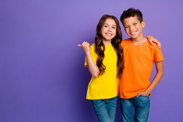 Photo of charming two little children hugging point empty space wear trendy orange yellow outfit isolated on violet color background