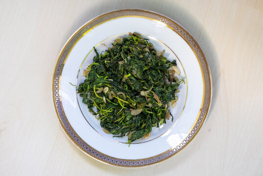 Stir-fried jute leaves, served in a white plate on a light wooden surface, are a nutritious green leafy vegetable known as pat shak in Bangladesh. Healthy diet concept. Top view.