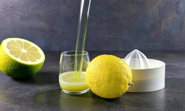 Jus de citron press&eacute; coulant dans un verre, avec un citron et un presse-agrumes en arri&egrave;re-plan, boisson fra&icirc;che et naturelle pleine de vitamine C