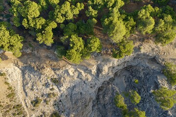 Aerial view of rocky cliffside surrounded by dense green pine trees at golden hour