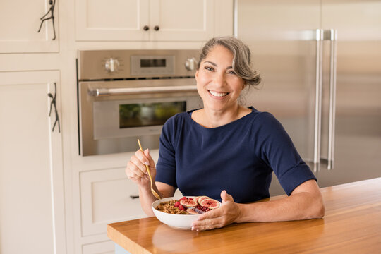 Woman smiling at camera with a bowl of yogurt in kitchen - Powered by Adobe