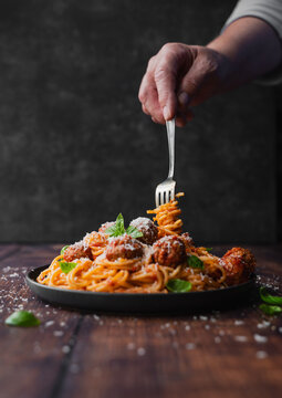 Hand twirling fork in plate of spaghetti and meatballs on table.