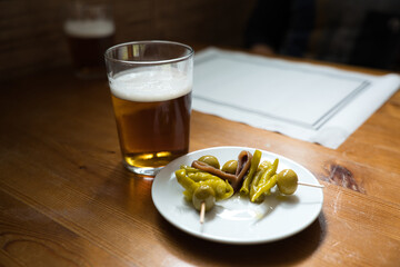 Glass of beer is standing on a wooden table next to a plate of olives, peppers and anchovies on a...