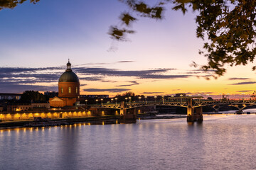 Fototapeta premium Golden sunset over Garonne river with views on the the pedestrian Saint-Pierre bridge, Place Saint-Pierre and the Grave hospital seen from the riverside 