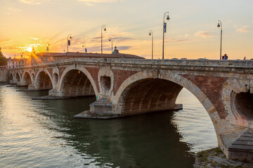 Golden sunset over the Garonne river and Pont Neuf in downtown Toulouse. This arch bridge is considered a masterpiece of the Renaissance. The bridge is not symmetrical.