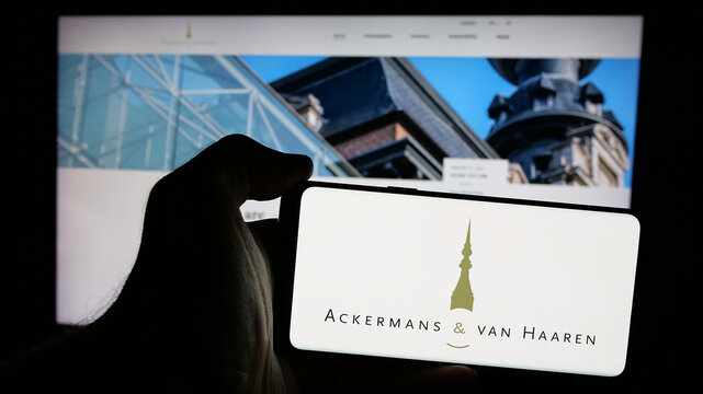 Stuttgart, Germany - 09-29-2024: Person holding mobile phone with logo of Belgian company Ackermans van Haaren NV on screen in front of business web page. Focus on phone display.