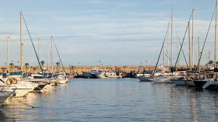 Fototapeta premium Sailing yachts and motor boats moored in a marina on a sunny day. Costa Blanca coastline, Villajoyosa, Alicante, Spain. Sea pier in old fishing harbor