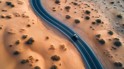 Obraz premium An aerial view of a winding desert road cutting through the endless stretch of sand dunes with a lone vehicle traveling down the road