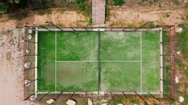 drone aerial view of an outdoor tennin or padle pitch with green, sandy ground, surrounded by stones and earth