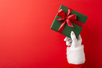 Close-up of Santa Claus hand holding a green gift with a red ribbon, symbolizing Christmas and...